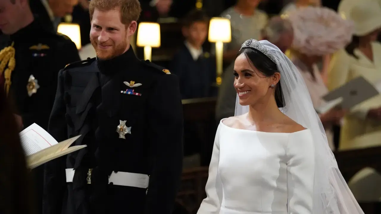 Meghan Markle y el Príncipe Harry sonríen en su boda. Ella luce un vestido blanco y él un uniforme militar.