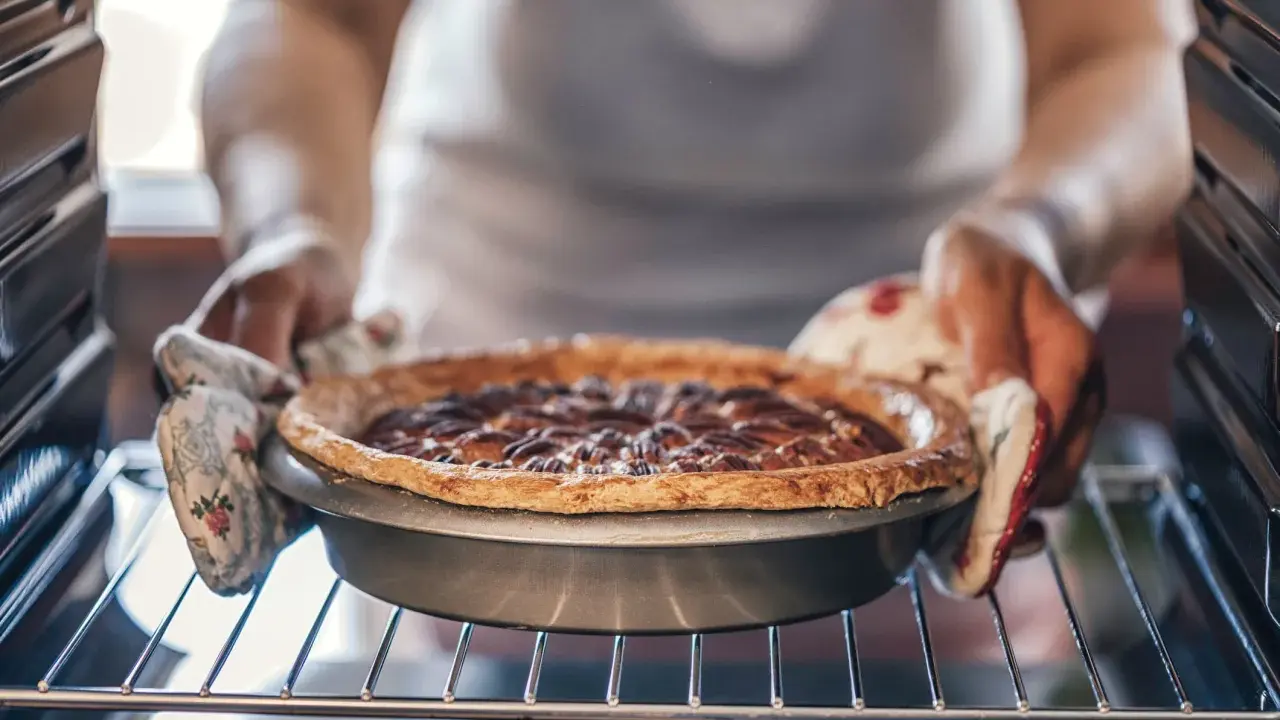 Hände mit Ofenhandschuhen nehmen einen frisch gebackenen Nusskuchen aus dem Ofen. Alles, was man zum Backen braucht: Zutaten, ein Rezept und Geduld.