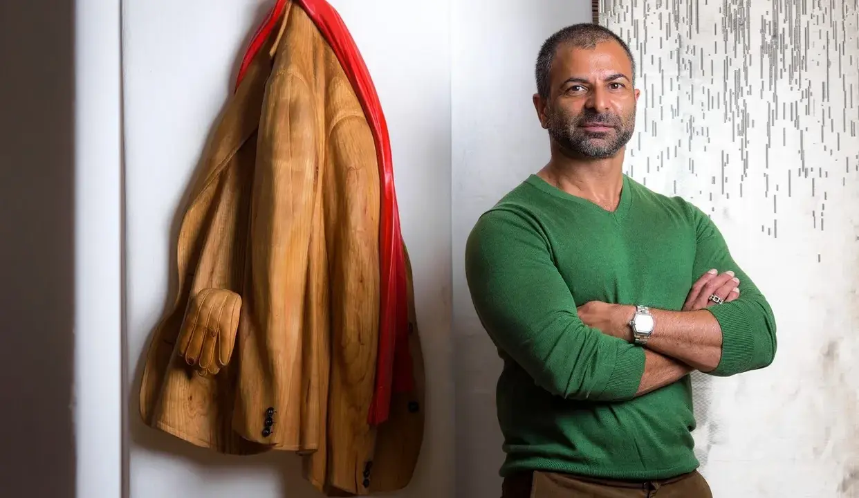 Livio De Marchi, artiste sculpteur, pose à côté de son manteau en bois sculpté, une œuvre saisissante.