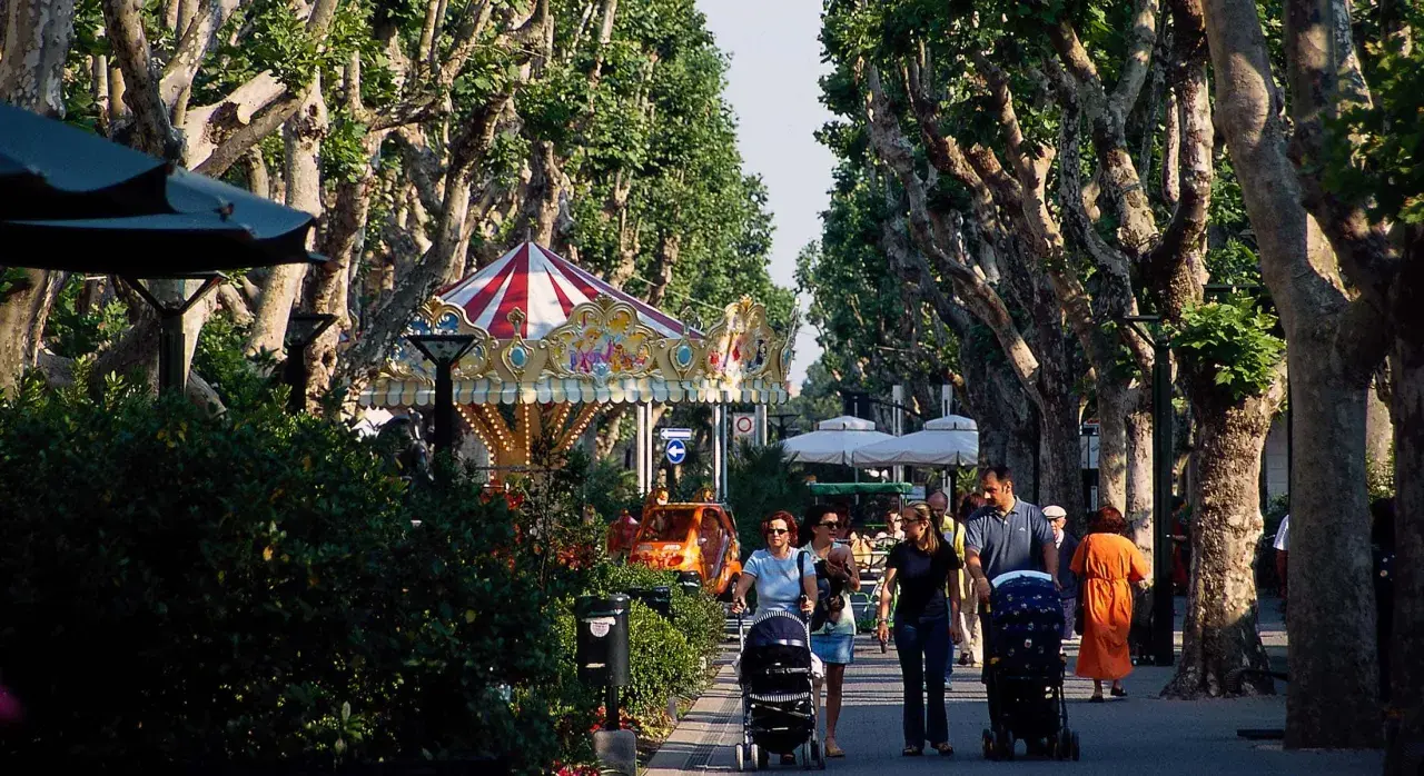 Passeggiata nel centro di Bellaria, con giostra, alberi maestosi e famiglie con passeggini.