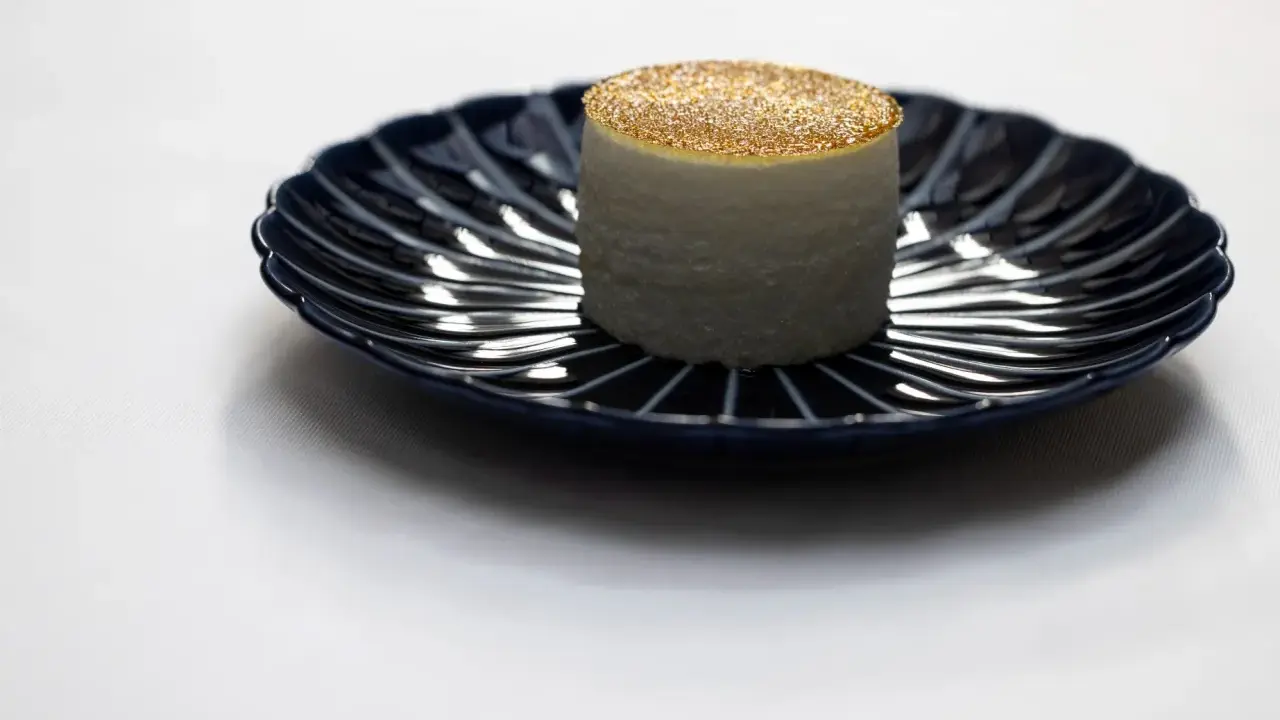 Un cylindre blanc, saupoudré d'or, sur une assiette bleue. Une idée de quoi manger à Paris pour une expérience culinaire unique.