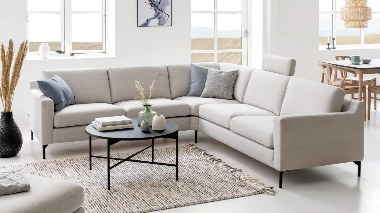En ljus, modern hörntyp av soffa med kuddar och ett runt soffbord framför.