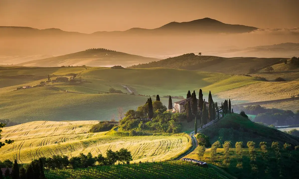 Dolci colline verdi e un casale con cipressi nel Val d'Orcia. Ideale da visitare in primavera o autunno per colori e luce perfetti.