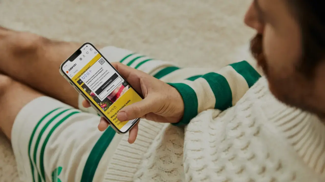 Mężczyzna sprawdza na telefonie, czy zalando jest legit, przeglądając aplikację z poradami stylistycznymi.