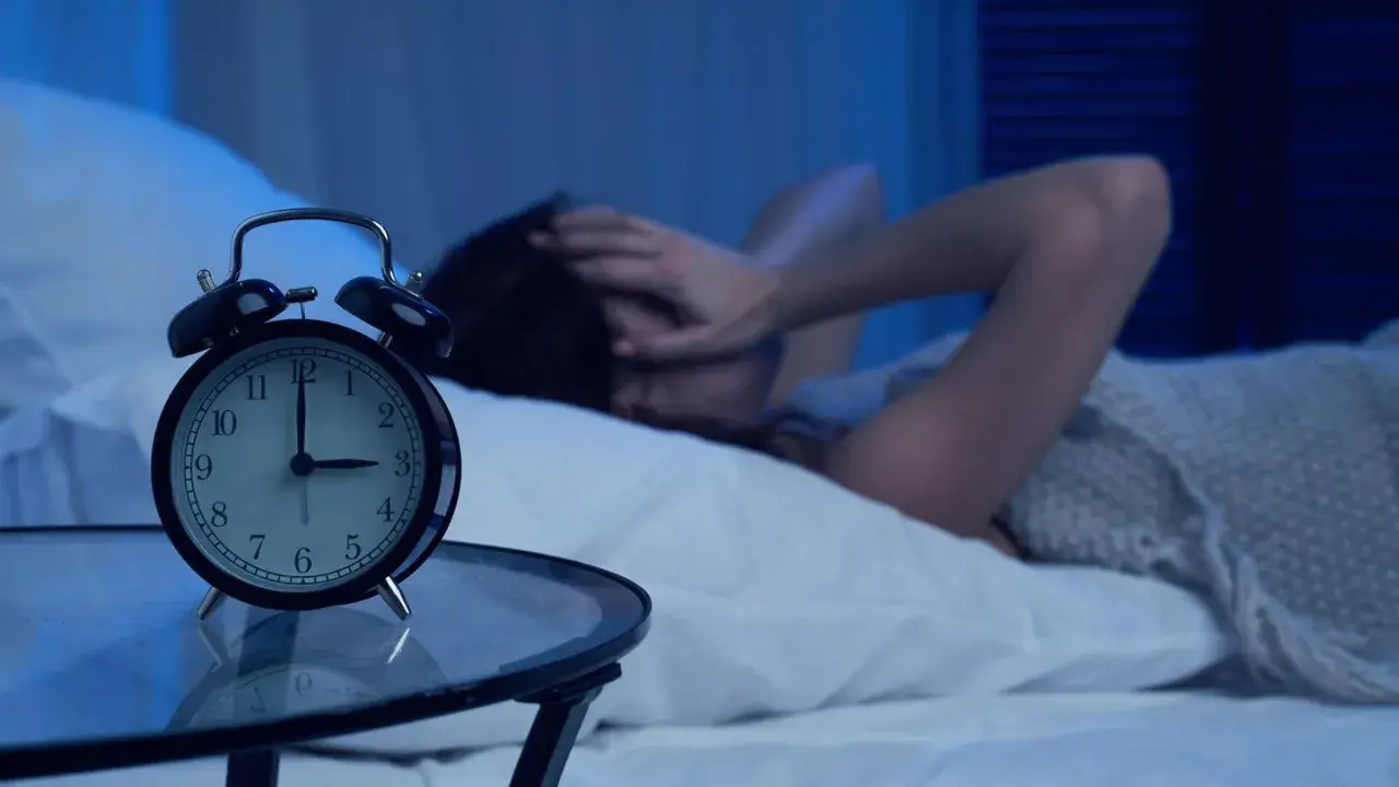 Eine Person liegt im Bett, die Hände über dem Gesicht, während ein Wecker auf 4 Uhr steht. Warum wache ich immer um 4 Uhr auf?