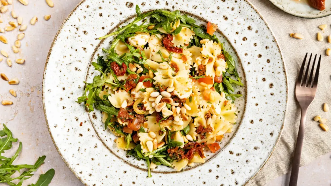 Ein köstlicher mediterraner Salat mit Farfalle, getrockneten Tomaten, Rucola und Pinienkernen.