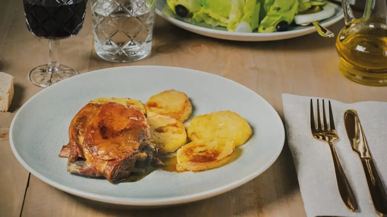 Plato de carne asada con patatas, un ejemplo de comida típica de Huesca. Acompañado de ensalada, vino tinto y aceite de oliva.