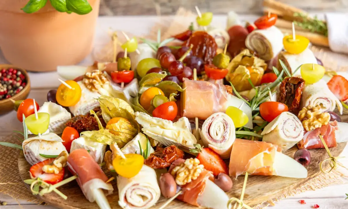 Bunte Platte mit Fingerfood-Dips: Prosciutto-Röllchen, Käse, Trauben, Tomaten, Physalis und Nüsse. Perfekt für jede Party!