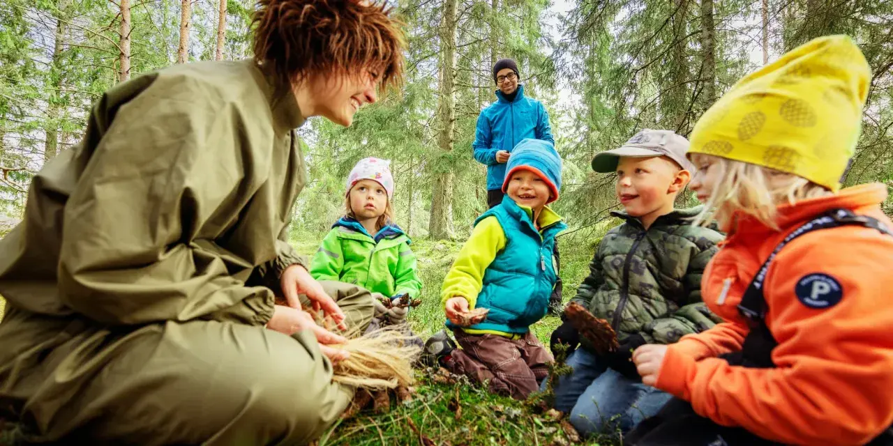 En grupp barn och en vuxen njuter av en dag i mulle skogen, omgivna av träd och grönskande natur.