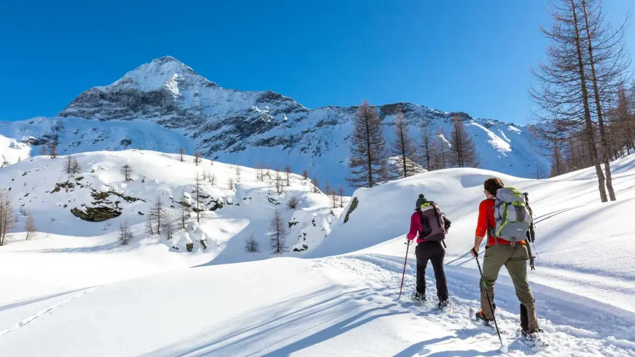 Coppia con ciaspole esplora un sentiero innevato in montagna, un'ottima idea per chi cerca dove ciaspolare in Lombardia.