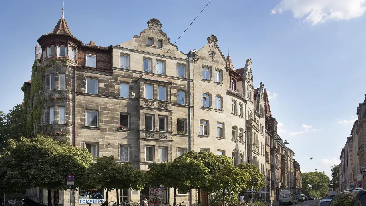 Ein prächtiges Jugendstil Haus mit Erker und Türmchen, umgeben von Bäumen, steht an einer belebten Straße.