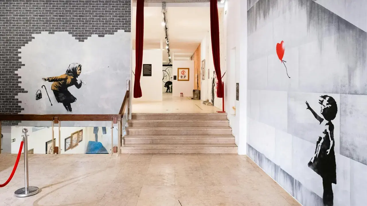 Banksy Lissabon: ikonische Werke wie das Mädchen mit dem roten Ballon und die wegspritzende Frau zieren die Wände einer Ausstellung.