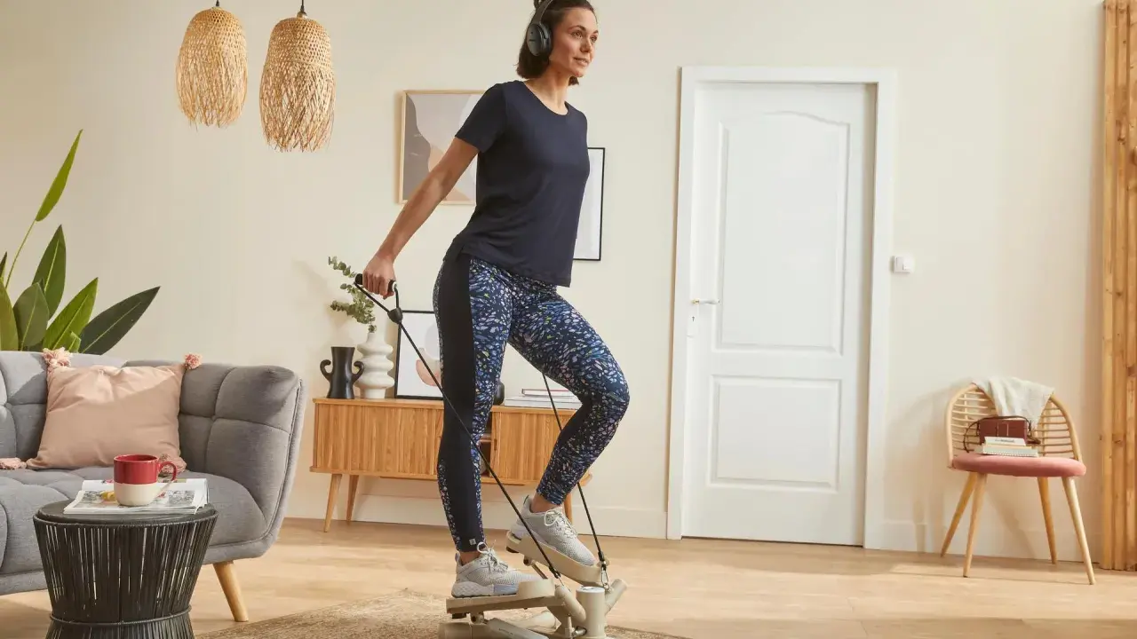 Une femme fait du step à la maison, casque sur les oreilles, pour un entraînement cardio efficace dans son salon.