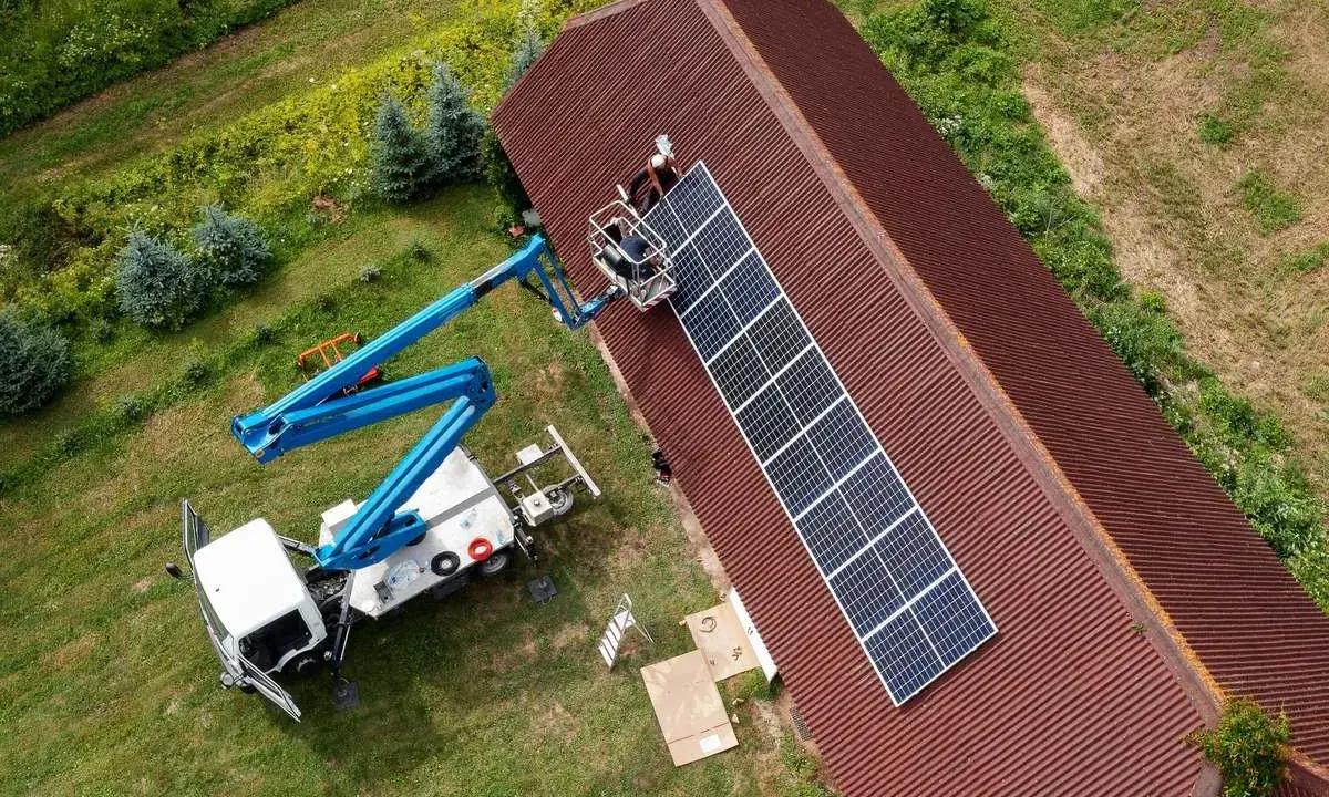 Installatörer monterar solpaneler på ett tak med hjälp av en kranbil. Solpaneler omvandlar solljus till likström (DC), som sedan kan omvandlas till växelström (AC) för användning i hemmet.