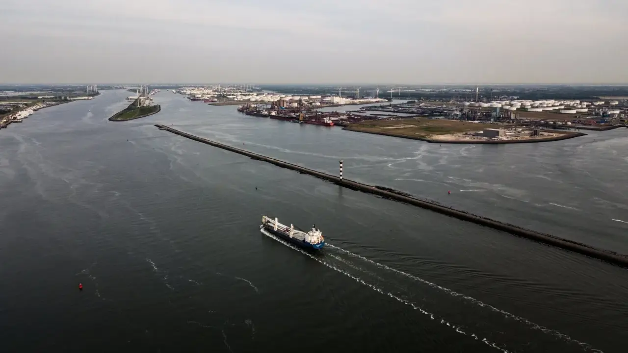 Una nave solca le acque di quello che è il più grande porto d'Europa, con industrie e serbatoi sullo sfondo.
