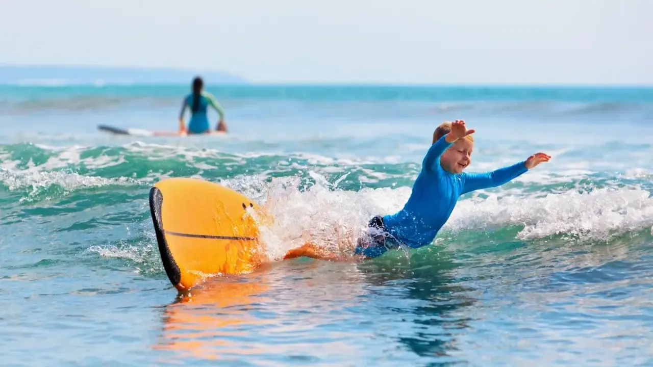 Niño sonriente surfeando en Portugal, una actividad genial que ver en Portugal con niños.
