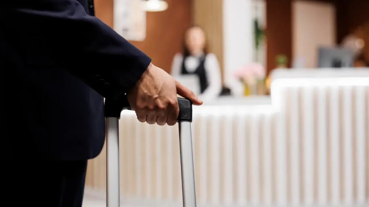 Mężczyzna w garniturze trzyma walizkę, zbliżając się do recepcji hotelowej. Czas na depozyt w hotelu i nowy początek podróży.
