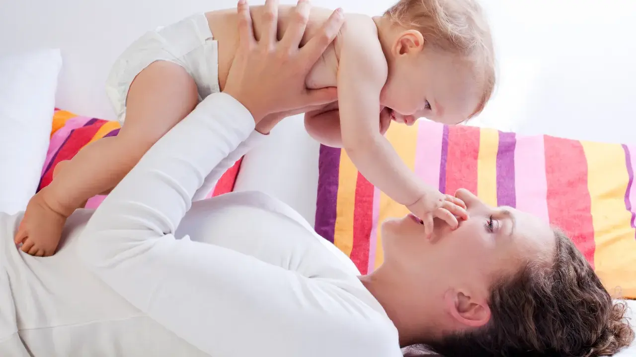 Mama podnosi dziecko, które wyciąga rączkę do jej nosa. Zdjęcie symbolizuje troskę o rozwój malucha, jak omega 3 dla niemowląt.