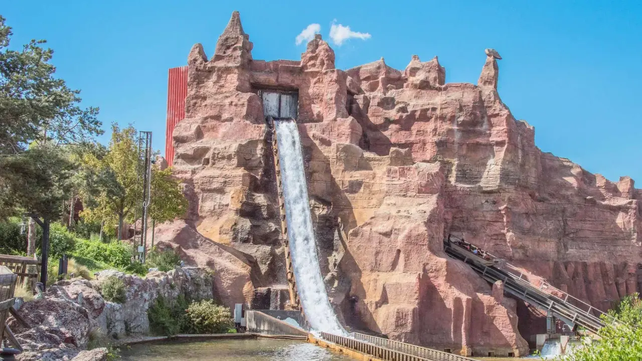Aventura acuática en uno de los parques de atracciones en España. Un tronco desciende por una cascada artificial en un paisaje rocoso.