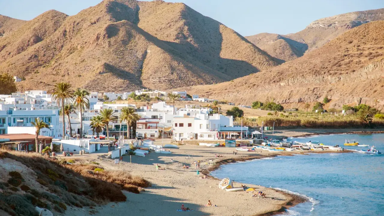 Pueblos de Almería con playa, casas blancas y palmeras junto a un mar azul, con montañas áridas de fondo.