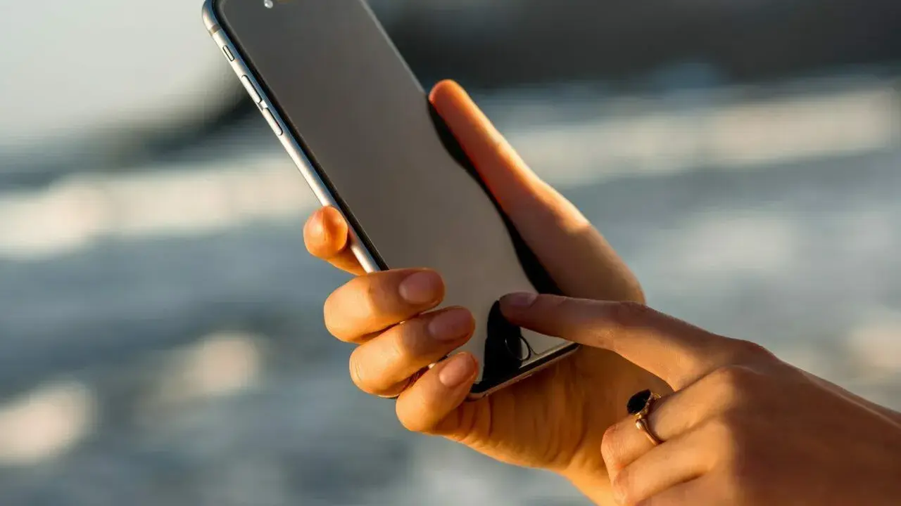 Dłoń trzyma iPhone 13, który nie chce się włączyć. Palec wskazujący próbuje go ożywić.