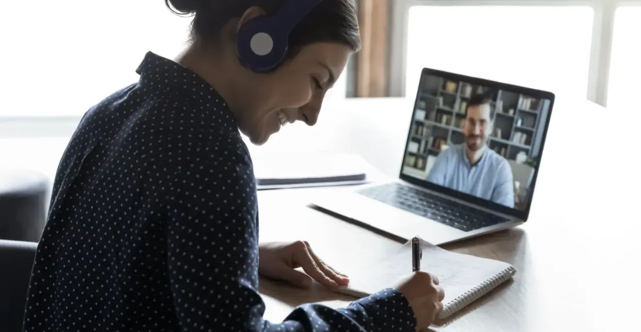 Ragazza con cuffie sorride mentre prende appunti durante una lezione online, comprendendo il vero e-learning significato.