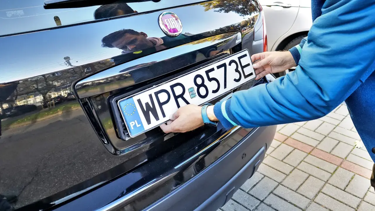 Mężczyzna montuje tablicę rejestracyjną. Pamiętaj o ważności dowodu rejestracyjnego, aby uniknąć problemów.