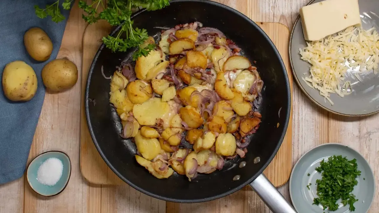 Bratkartoffeln rezept: goldbraune Kartoffeln mit Zwiebeln und Käse in der Pfanne, dazu frische Petersilie und Salz.