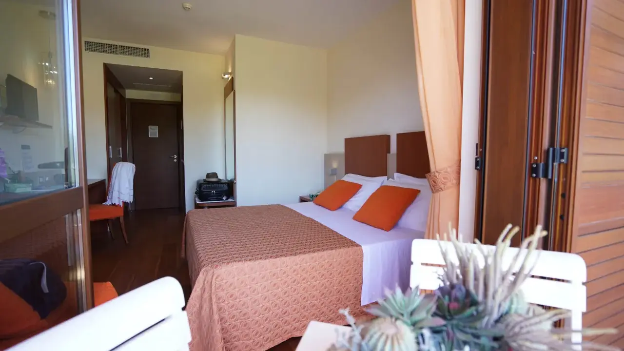 Camera accogliente al Valtur Otium Resort, con letto comodo, cuscini arancioni e vista sulla porta scorrevole in legno.