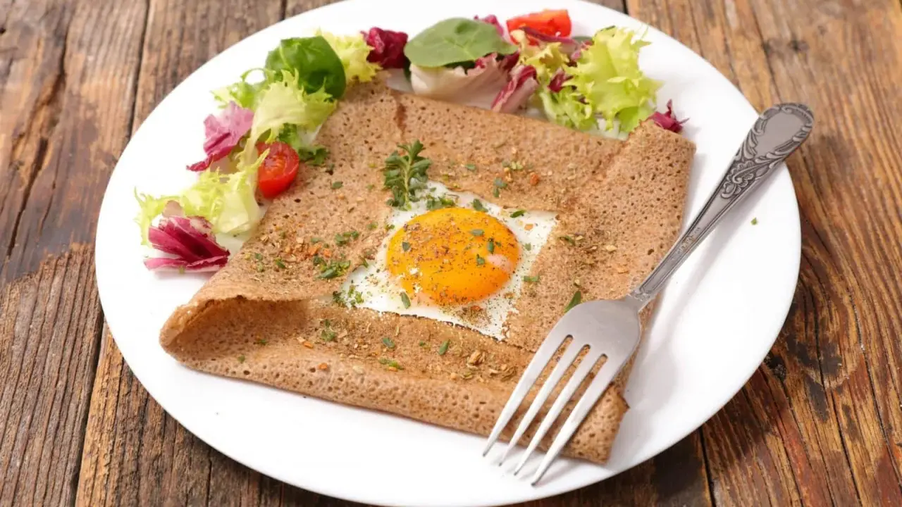 Galette bretonne complète au four, garnie d'un œuf au plat, d'herbes et servie avec une salade fraîche.