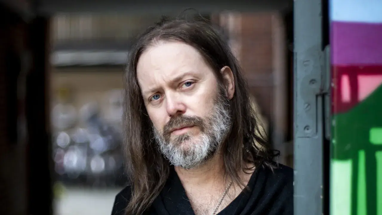 Niclas Frisk med långt hår och skägg, blickar mot kameran.