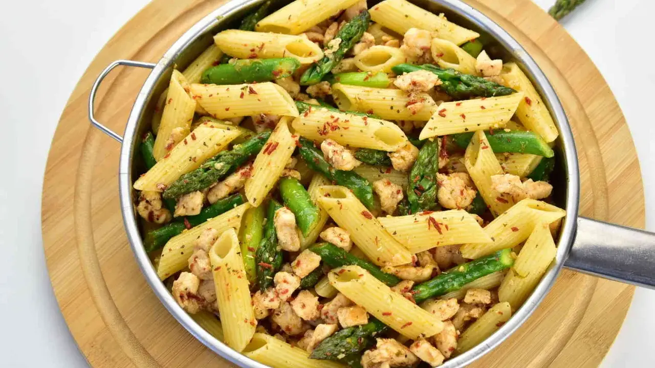 Penne z kurczakiem i szparagami, posypane płatkami chili. Pyszne danie na szybki obiad.
