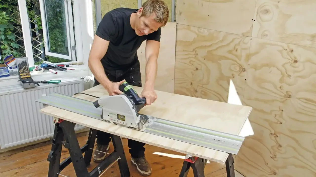 Man spacklar plywood med en cirkelsåg på en skena.