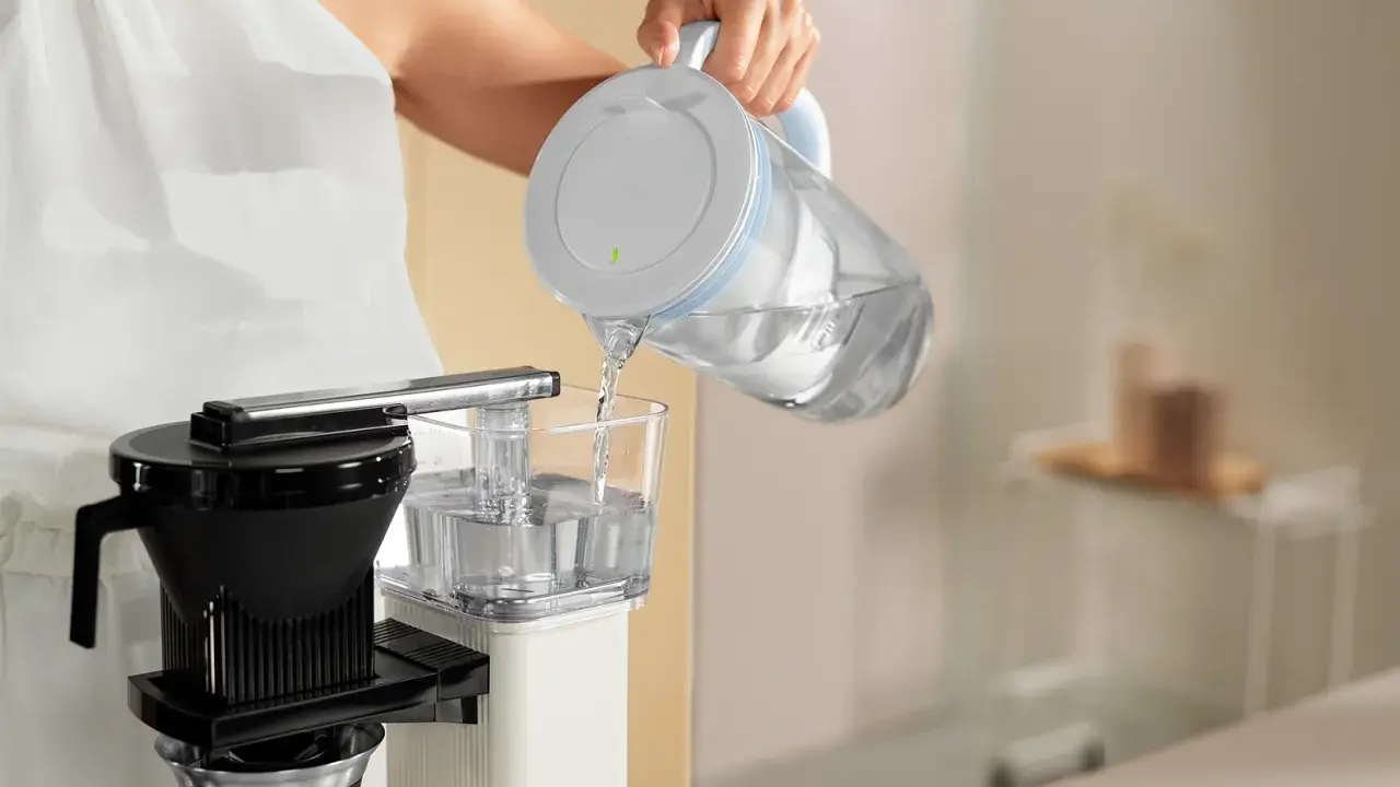 Eine Person füllt Wasser in eine Filterkaffeemaschine, um sie zu entkalken.