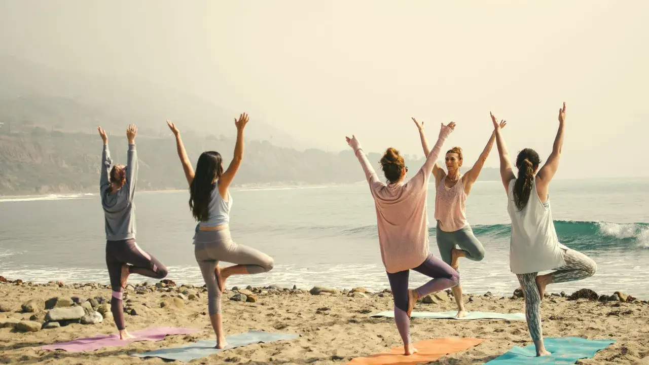 Kvinnor i trädposition på stranden. En lugn morgon för yoga, kanske en paus från pilates.
