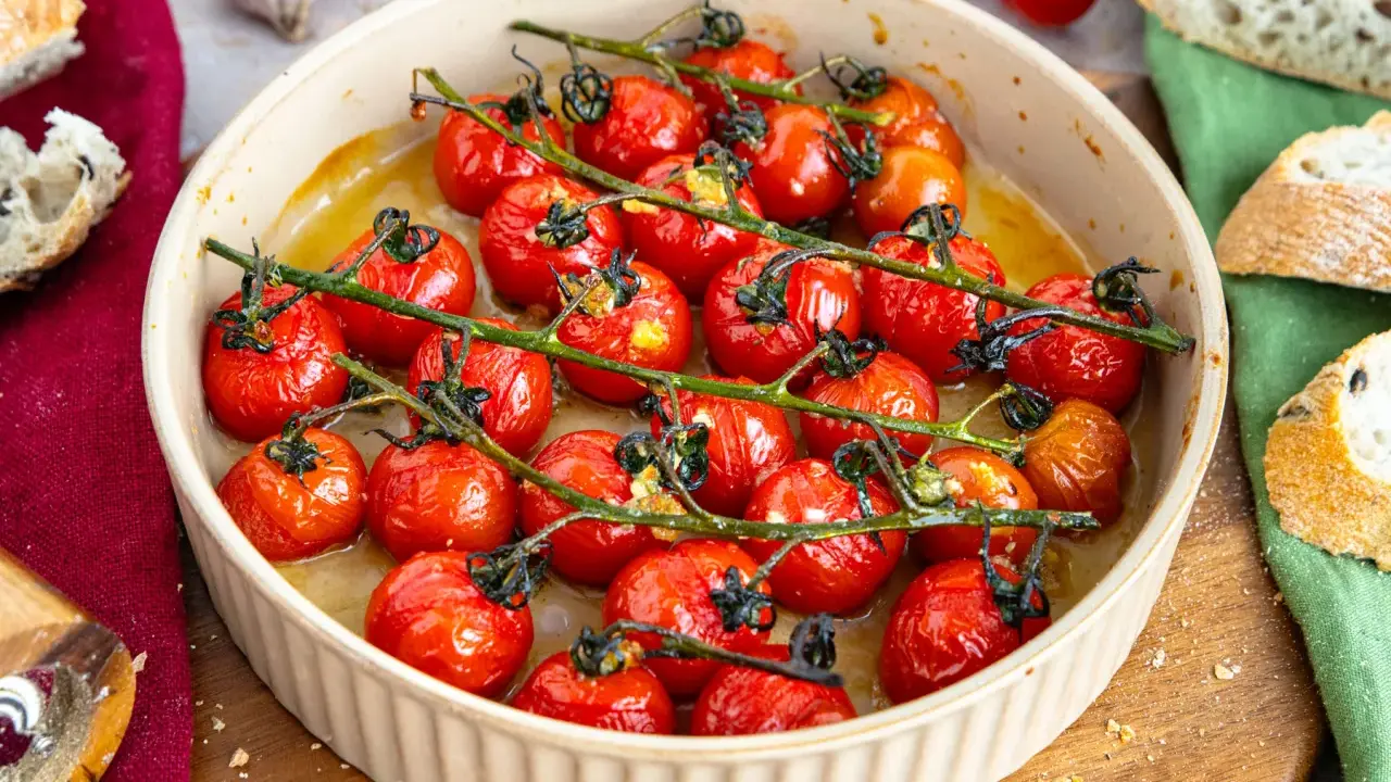 Konfierte Tomaten in einer Auflaufform, mit Brot und Knoblauch daneben.