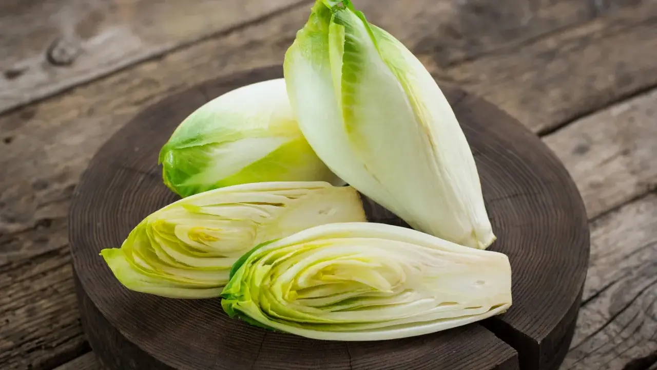 Frische Chicorée-Köpfe, einer davon halbiert, liegen auf einem Holzbrett. Perfekt für einen knackigen Chicorée-Salat.