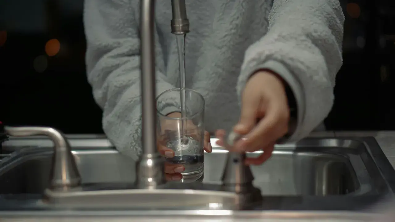 Mano llenando un vaso con agua del grifo, un problema común con el agua dura en España.
