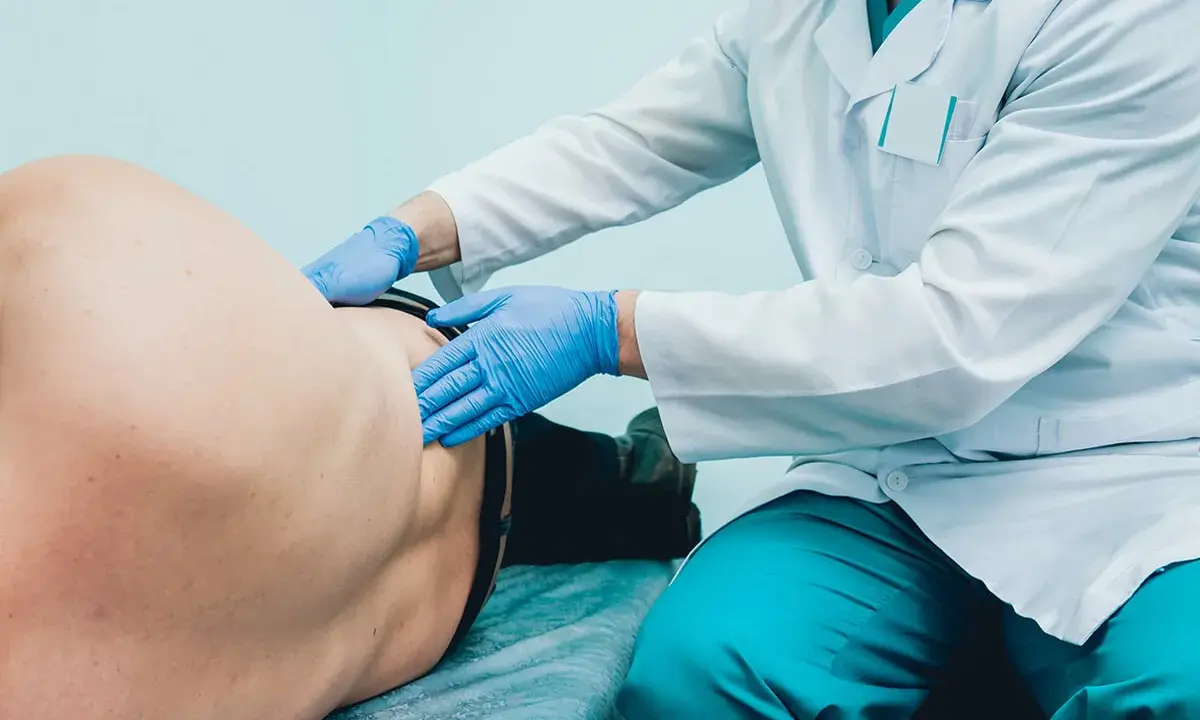 Lekarz od pęcherza w niebieskich rękawiczkach bada pacjenta leżącego na kozetce.