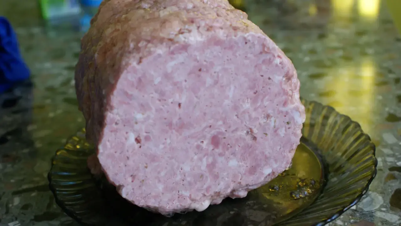 Pokrojona mielonka z szynkowara, różowa i soczysta, leży na ciemnej, karbowanej paterze.