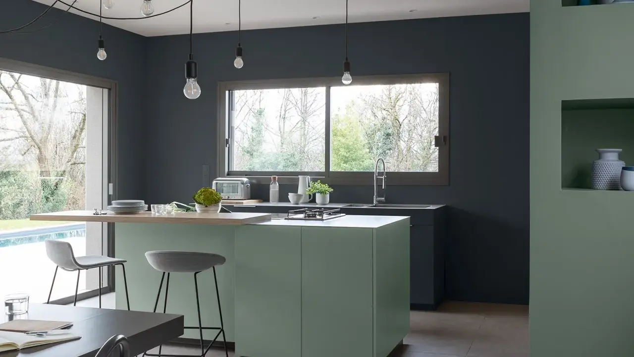 Cuisine moderne aux murs gris anthracite. L'îlot central vert sauge et le plan de travail en bois clair invitent à la convivialité. Quelle peinture pour plafond ? Un blanc mat pour agrandir l'espace.