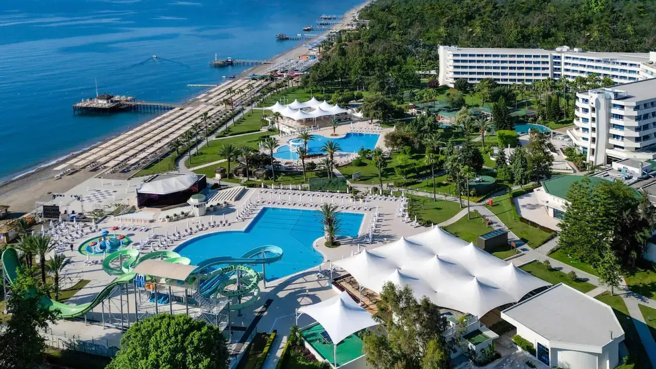 Widok z lotu ptaka na Mirage Park Resort: plaża, baseny, zjeżdżalnie wodne, białe pawilony i hotele otoczone zielenią.