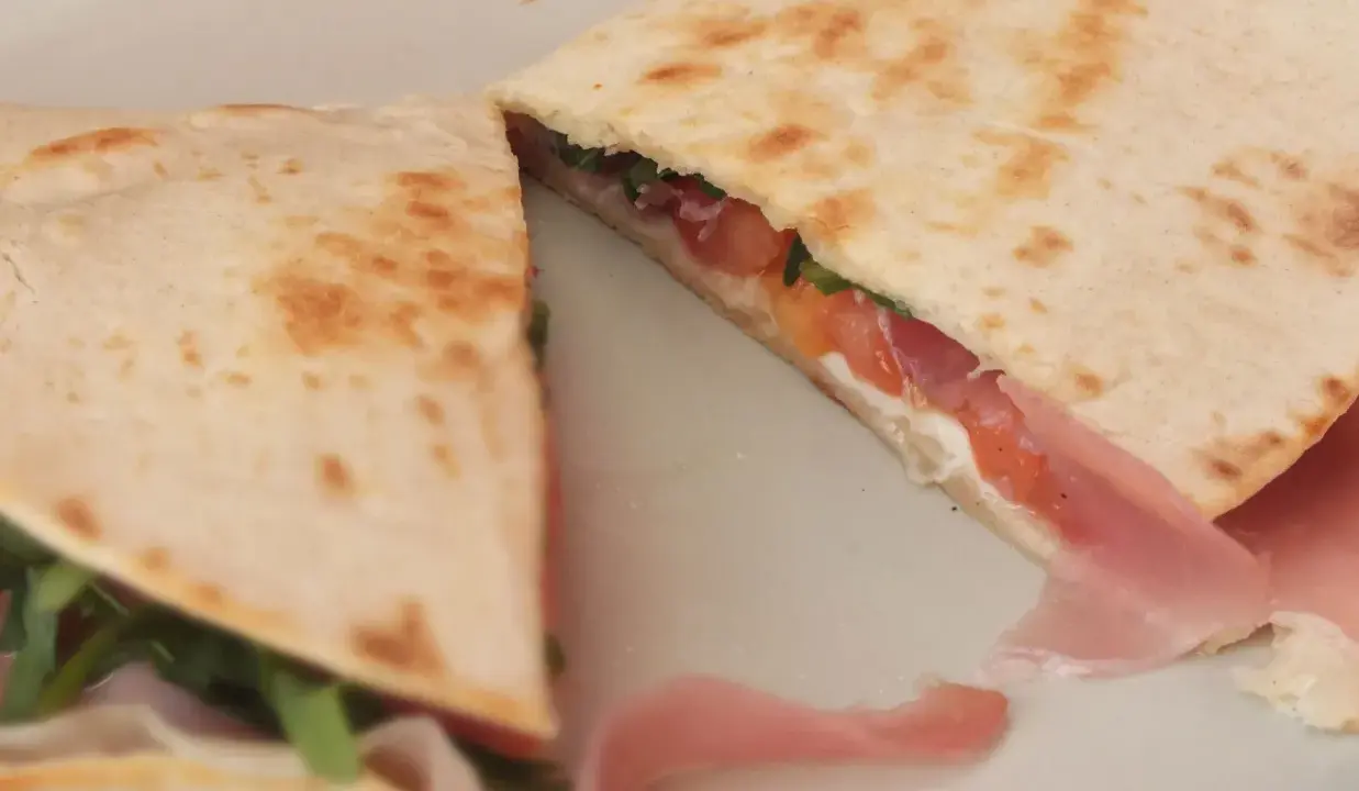 Pyszna piadina z szynką, pomidorami i rukolą, złożona na pół, prezentuje apetyczny przekrój.