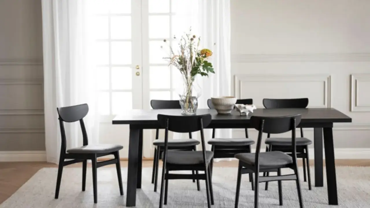 Svart matbord med sex stolar, en vas med blommor och en skål. Modern inredning matplats med ljus matta och vita dörrar i bakgrunden.