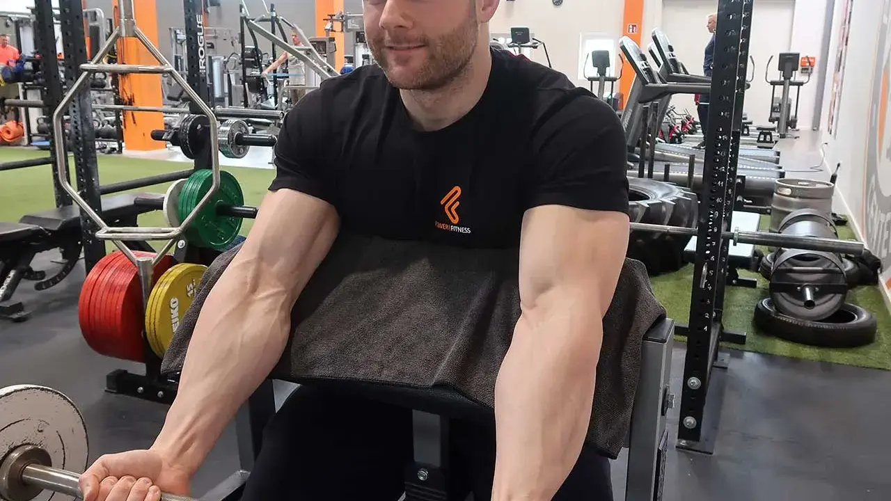 Mann trainiert Bizeps mit Langhantel im Fitnessstudio. Deutlich sichtbare Muskeln beim Bizeps dehnen.
