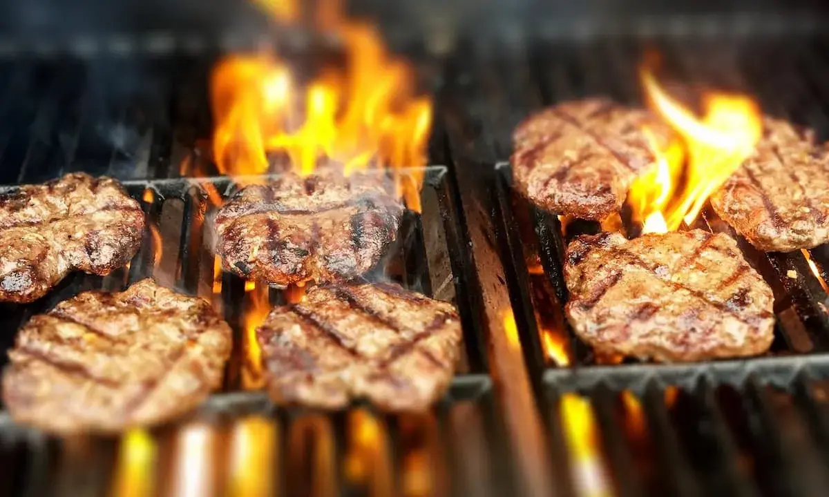 Flera saftiga hamburgare grillas över öppna lågor. Doften av sommar och grillning sprider sig.