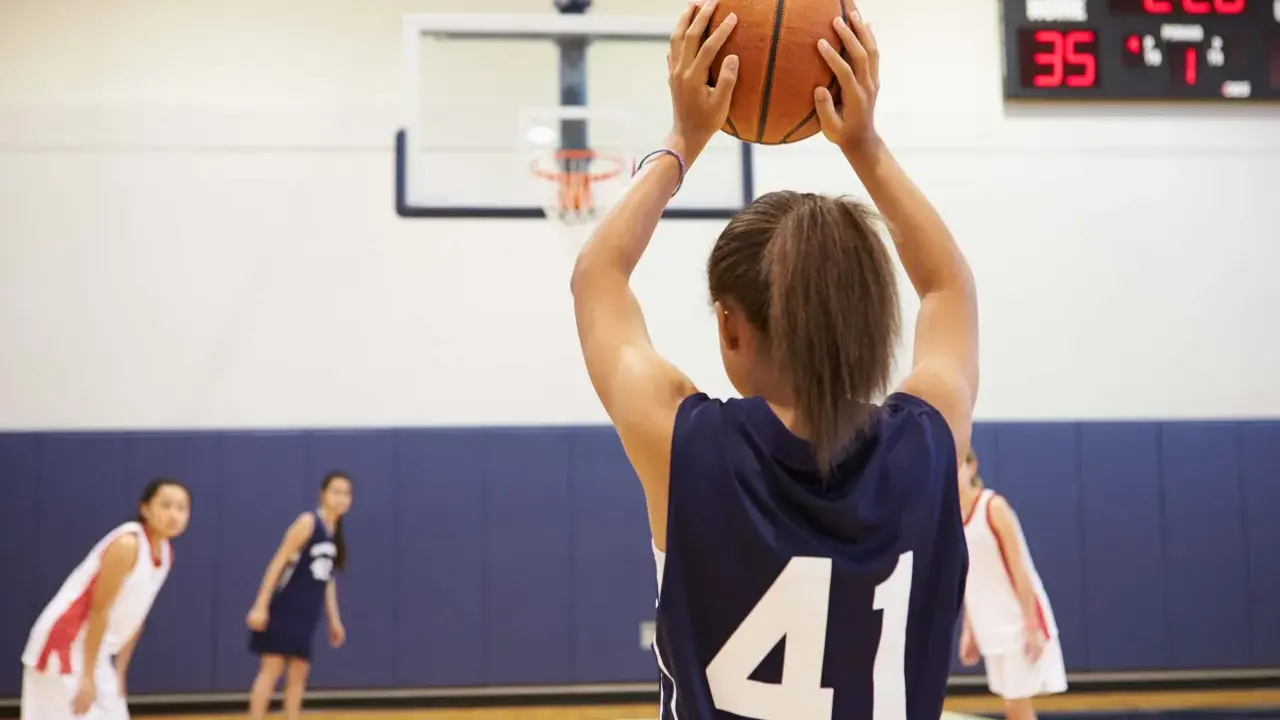 Ragazza con palla da basket, un ottimo sport per bambini iperattivi. In campo, altre giocatrici si preparano.