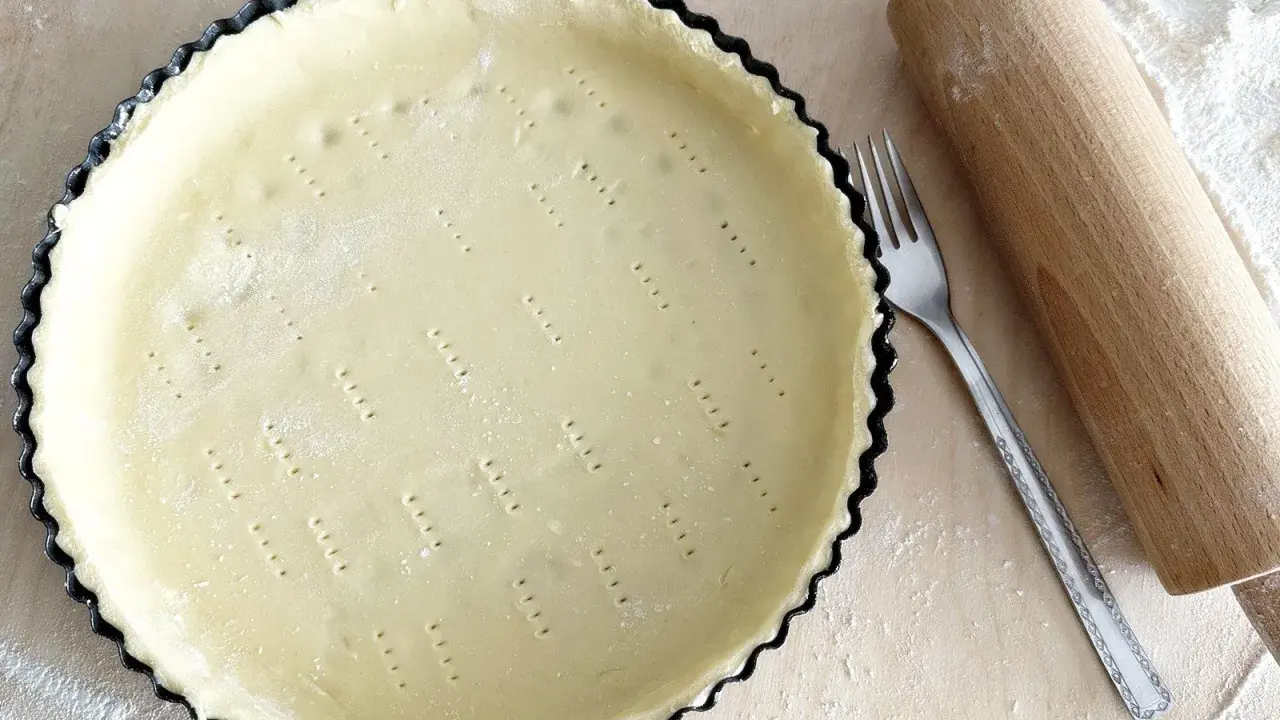 Surowe ciasto wegańskie w formie do tarty, obok wałek i widelec. Gotowe do pieczenia pysznego deseru.