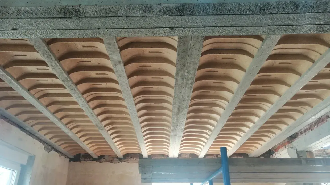 Widok od dołu na betonowe belki stropowe i pustaki ceramiczne, ukazujące różne rodzaje stropów w trakcie budowy.