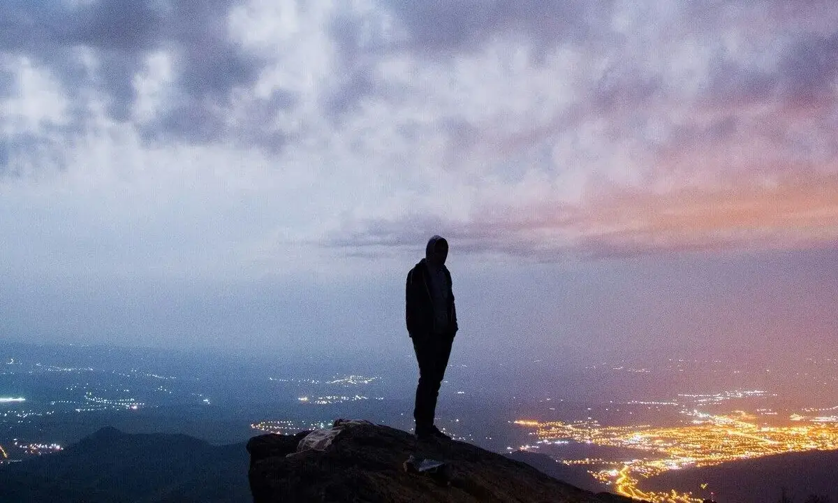 Silhouette di una persona su una rupe, con una città illuminata in lontananza. Un momento che fa amarcord, pensando a chi siamo e dove andiamo.